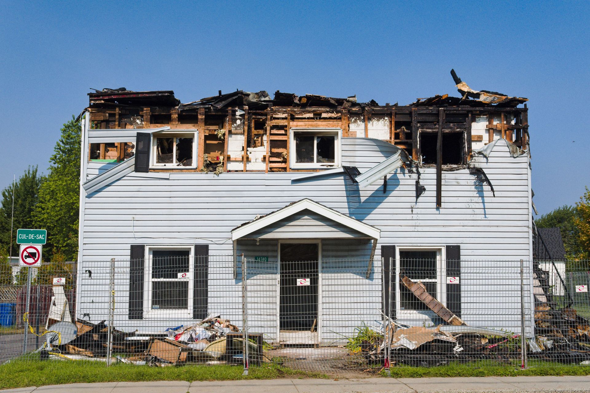 A damaged house with a burnt roof in Bécancour, Quebec, surrounded by a fence.